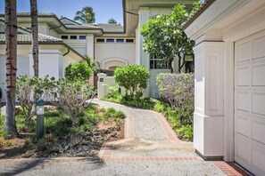 Stroll through the beautifully maintained garden, surrounded by lush plants and shrubs, to an entrance with a garage door.