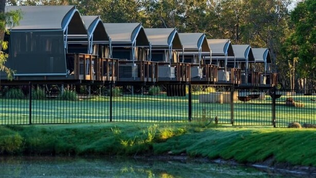 A row of modern, semi-open cabins with a reflective water body in the foreground. - Splitters Farm (Sharon)