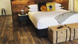 A bedroom with a wooden headboard, a bed with white bedding, two bedside lamps, a nightstand, and wicker storage baskets. - Splitters Farm (Sharon)
