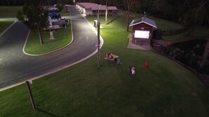 A well-maintained grassy area with a small building, possibly a restroom or utility room, near a road with parked vehicles. - Splitters Farm (Sharon)