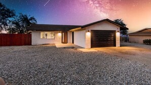 A house with a gravel driveway, a garage, and a night sky with stars and the Milky Way. - New 20% discount - Backyard PARADISE - JT Escape w/ Hot Tub (Joshua Tree)