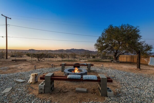 A fire pit with seating, surrounded by gravel, with a tree and mountains in the background.