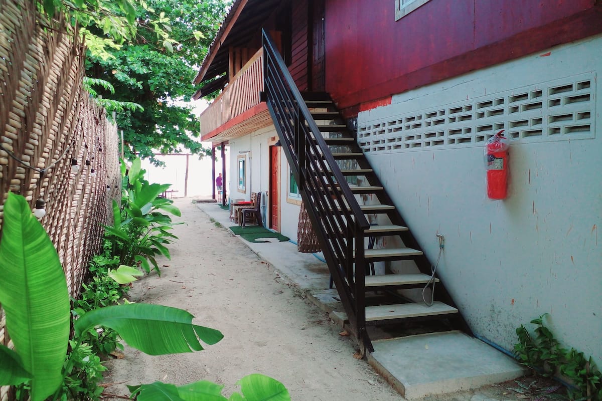 A narrow pathway leading to a building with a red exterior and a black staircase.