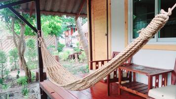 A hammock on a wooden deck with a view of a garden and a building in the background.