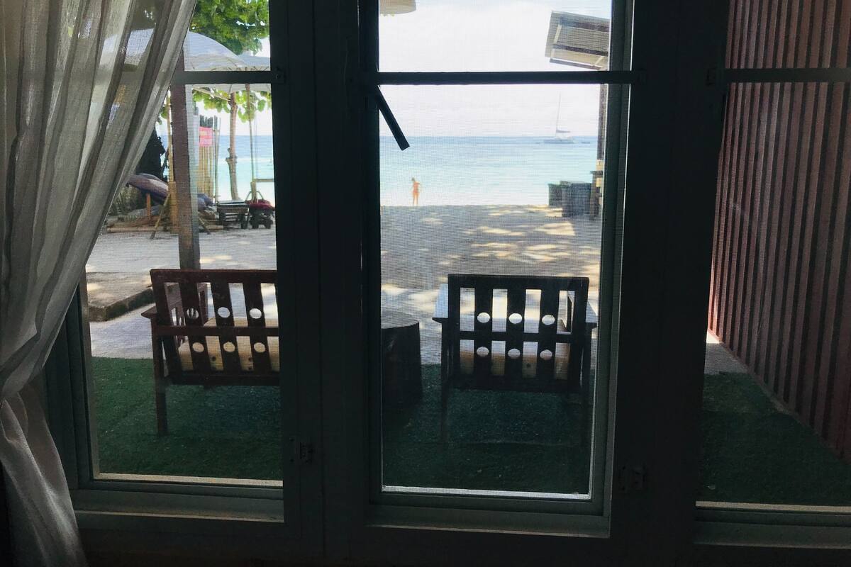 A view through a window with a wooden bench outside, a railing, and a clear sky.