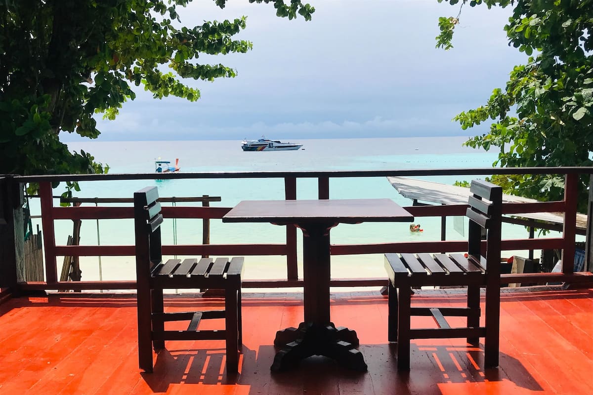 A wooden deck with a table and chairs overlooking a calm sea with boats.