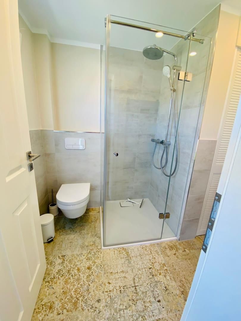 A modern bathroom with a glass-enclosed shower, a toilet, and a marble floor.
