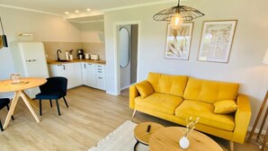 Una sala de estar moderna con un sofá amarillo, un comedor con una mesa redonda y una cocina al fondo.
