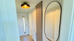 Un pasillo con suelo de madera, una lámpara en el techo, un espejo adosado a la pared y un radiador.