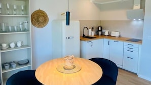 Una cocina moderna con armarios blancos, una lámpara colgante negra y una zona de comedor con dos sillas y una mesa redonda.
