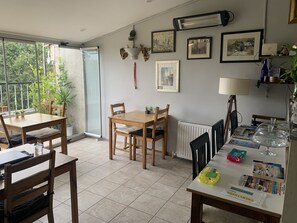A dining area with a table, chairs, and a radiator. There are framed pictures on the wall and a window with a view of greenery. - antik sofia hotel (Istanbul)