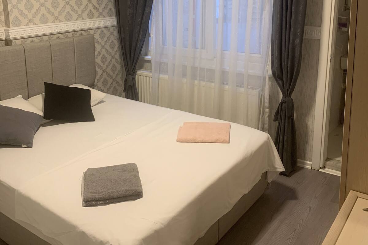 Una habitación de hotel con una cama grande, un radiador, una ventana con cortinas y una puerta.
