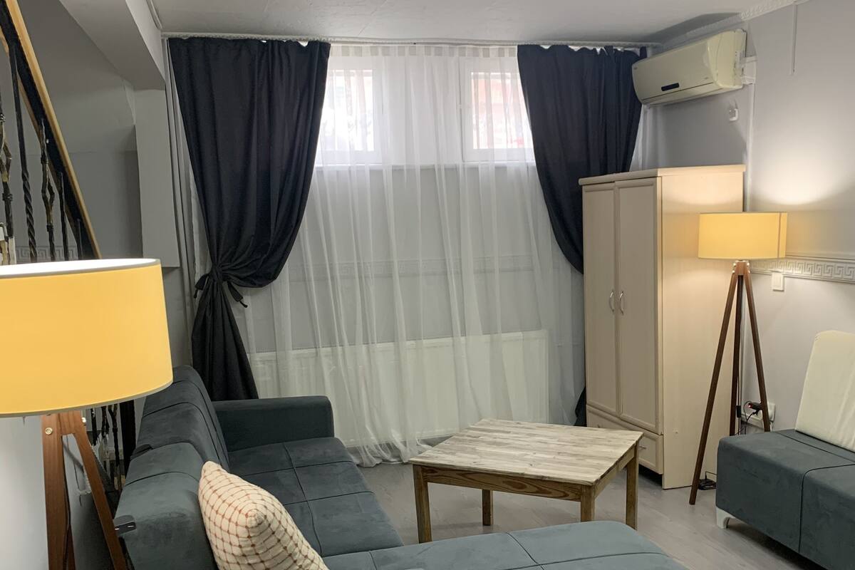 Una sala moderna con un sofá modular, una mesita de madera, una lámpara y un armario.