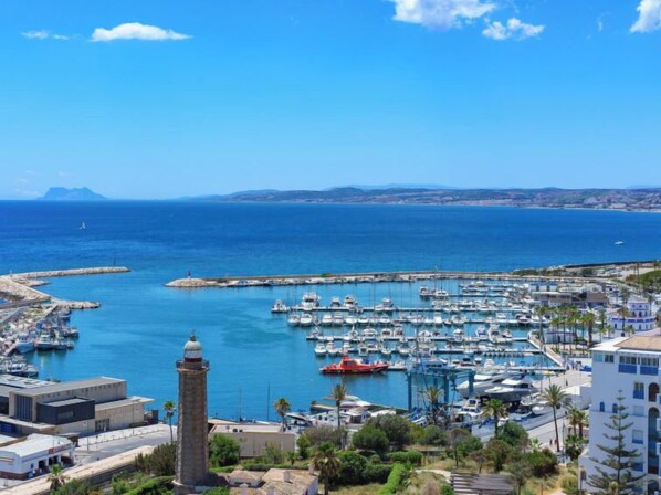 Un puerto costero con barcos, un faro y edificios de estilo mediterráneo.