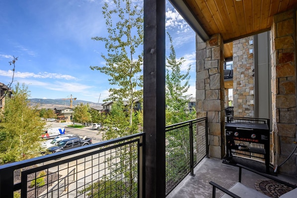 A balcony with a stone wall, a grill, and a view of a residential area with cars and trees.