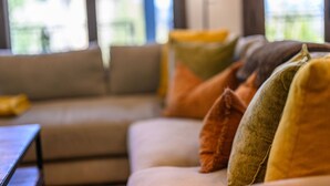 Um sofá com várias almofadas em um quarto com janelas amplas.