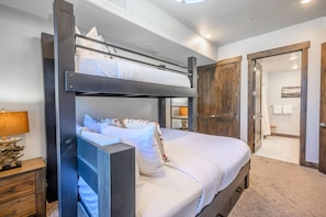 A bunk bed with a lower bunk, a bedside table with a lamp, and a wooden door leading to a bathroom.
