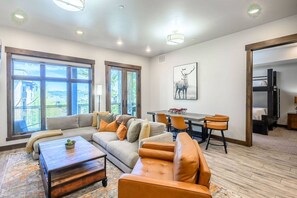 A spacious living area with a large window, a sofa, a coffee table, and a dining table with chairs.