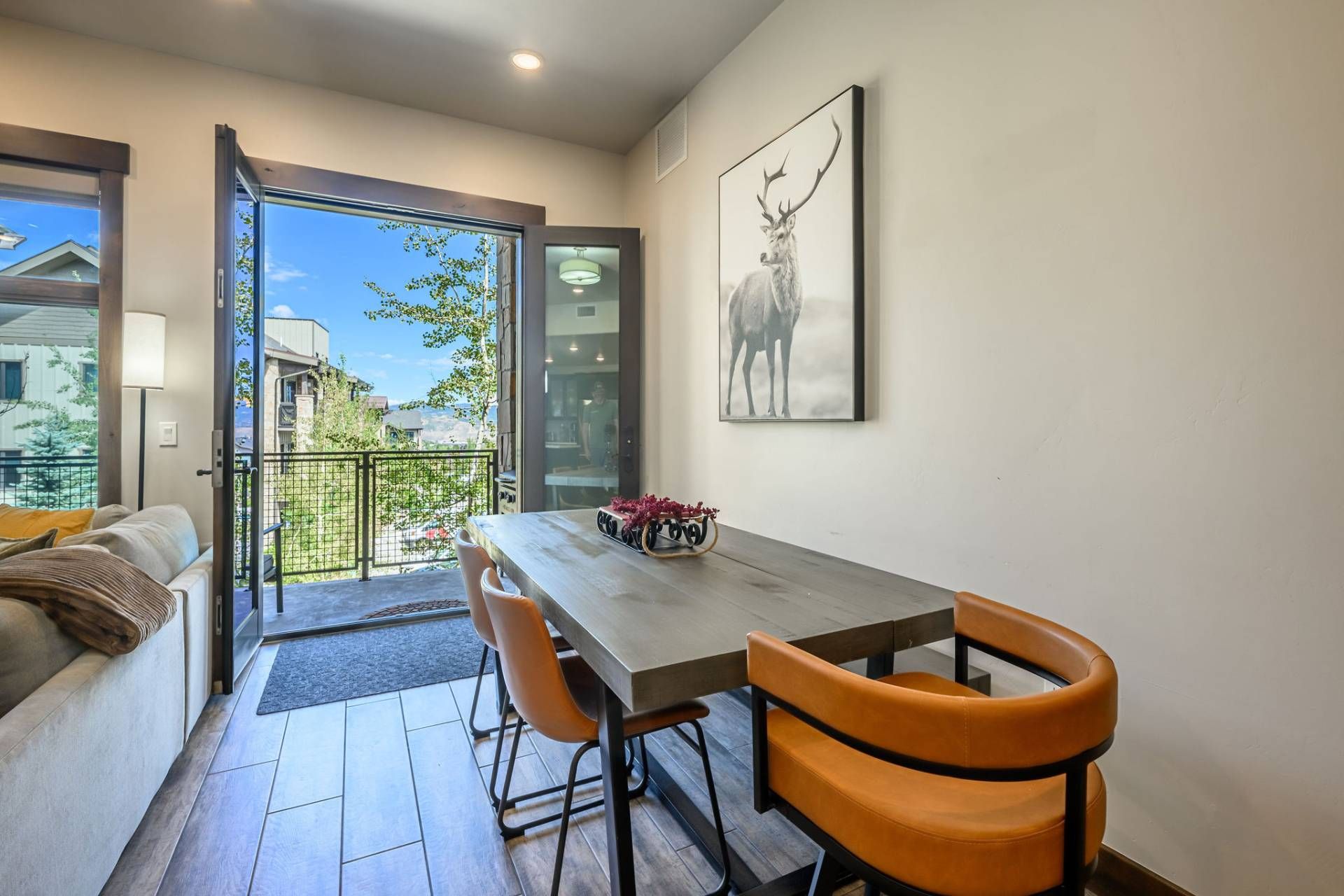 A dining area with a table and chairs, a view through a glass door, and a framed picture on the wall.