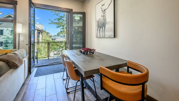 Uma área de refeições com mesa e cadeiras, vista através de uma porta de vidro e um quadro na parede.