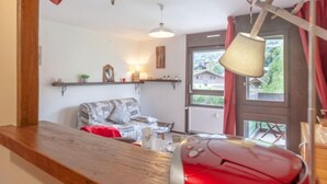 Een gezellige woonkamer met een houten bankje, een rode modelauto, en een raam met uitzicht op huizen.