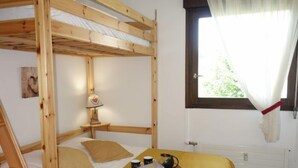 Een slaapkamer met een stapelbed met houten frame, een nachtkastje met lamp, een raam met gordijnen, en een dienblad met spullen op het bed.