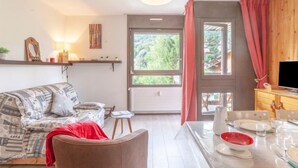 Een gezellige woonkamer met een bank, een eettafel gedekt voor twee personen, en een televisie op een houten kast.