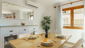 A dining area with a wooden table, white chairs, a vase with a plant, and a window with curtains. - Can Llorenc Sea Views by Interhome (Port d'Alcúdia)