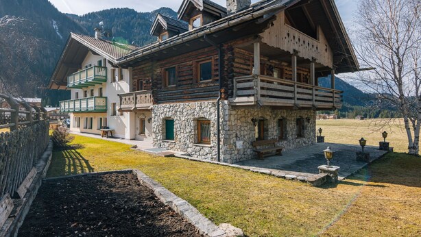 Un chalet traditionnel avec une façade en pierre, des balcons en bois et une cheminée en pierre.