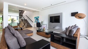 Een moderne woonkamer met een bank, salontafel en televisie. Een trap leidt naar een andere kamer.