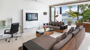 Een moderne woonkamer met een bank, een stoel, een televisie en een balkon met uitzicht op zee.