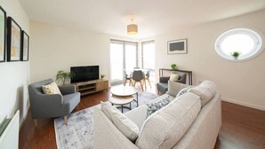 Una sala de estar moderna con sofá, sillones, televisor y comedor con sillas y mesa.
