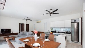 A modern kitchen with a refrigerator, dining table, and chairs. There is a living area with a sofa and a television. - Miami-Style 2BR Pool Villa Janine Kamala (Kamala)