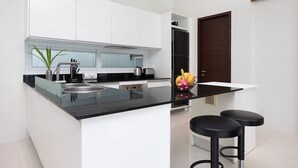 A modern kitchen with white cabinets, a black countertop, and two black bar stools. - Miami-Style 2BR Pool Villa Janine Kamala (Kamala)