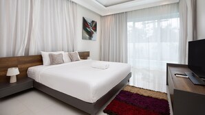 A modern bedroom with a large bed, a nightstand, a TV, and a window with sheer curtains. - Miami-Style 2BR Pool Villa Janine Kamala (Kamala)