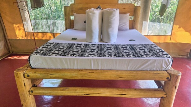 A bed with a patterned bedspread, pillows, and a wooden headboard. - Tindiga Tented Camp (Mangola)