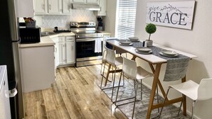A modern kitchen with white cabinets, a stainless steel oven, and a dining area with a marble table and white chairs.