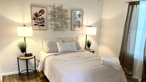 A neatly arranged bedroom with a bed, two bedside tables, a clock, and framed artwork on the wall.