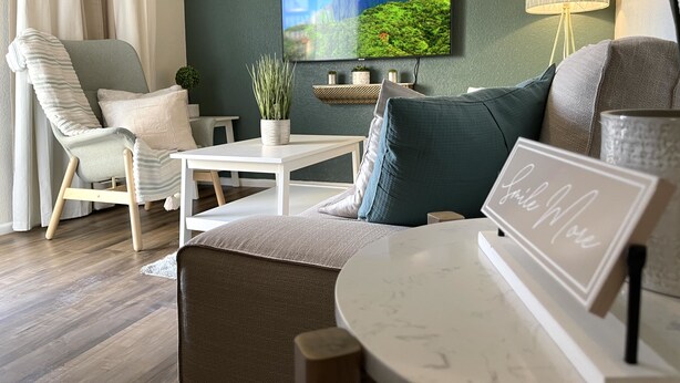 A living room with a modern design, featuring a sofa, a chair, a coffee table, and a flat-screen TV mounted on the wall.