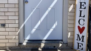 A white door with the number 1, a doormat with "hello", and a 'WELCOME' sign with a heart.