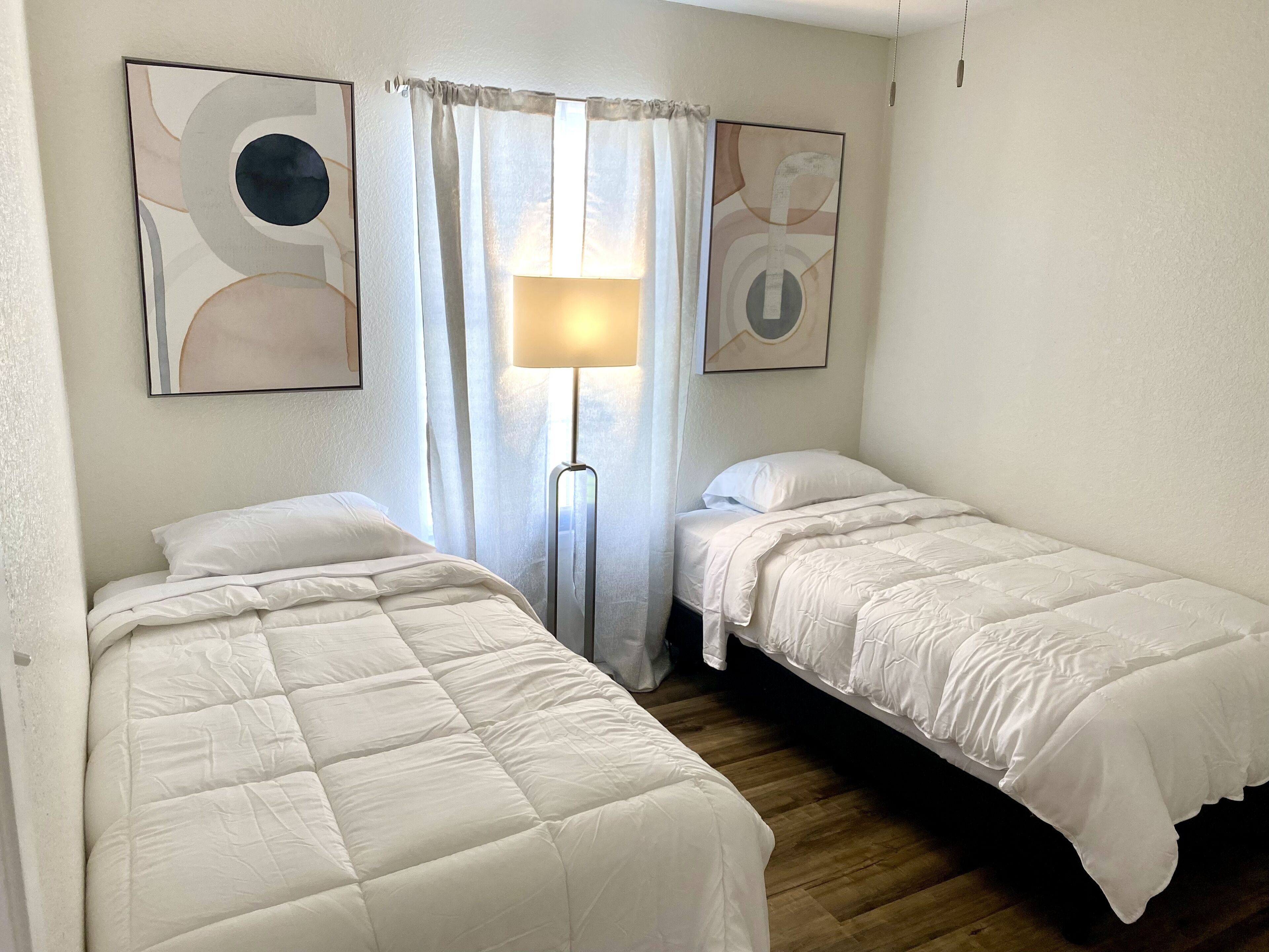 A room with two single beds, a floor lamp, and abstract wall art.