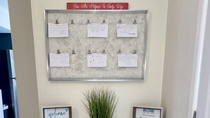 A reception desk with a bulletin board displaying handwritten notes, a welcome sign, and a small potted plant.