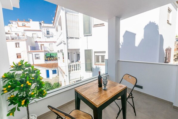 A balcony with a table, chairs, a potted plant, and a bottle of wine.