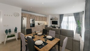 Uma sala de estar moderna com área de jantar, cozinha e TV na parede.