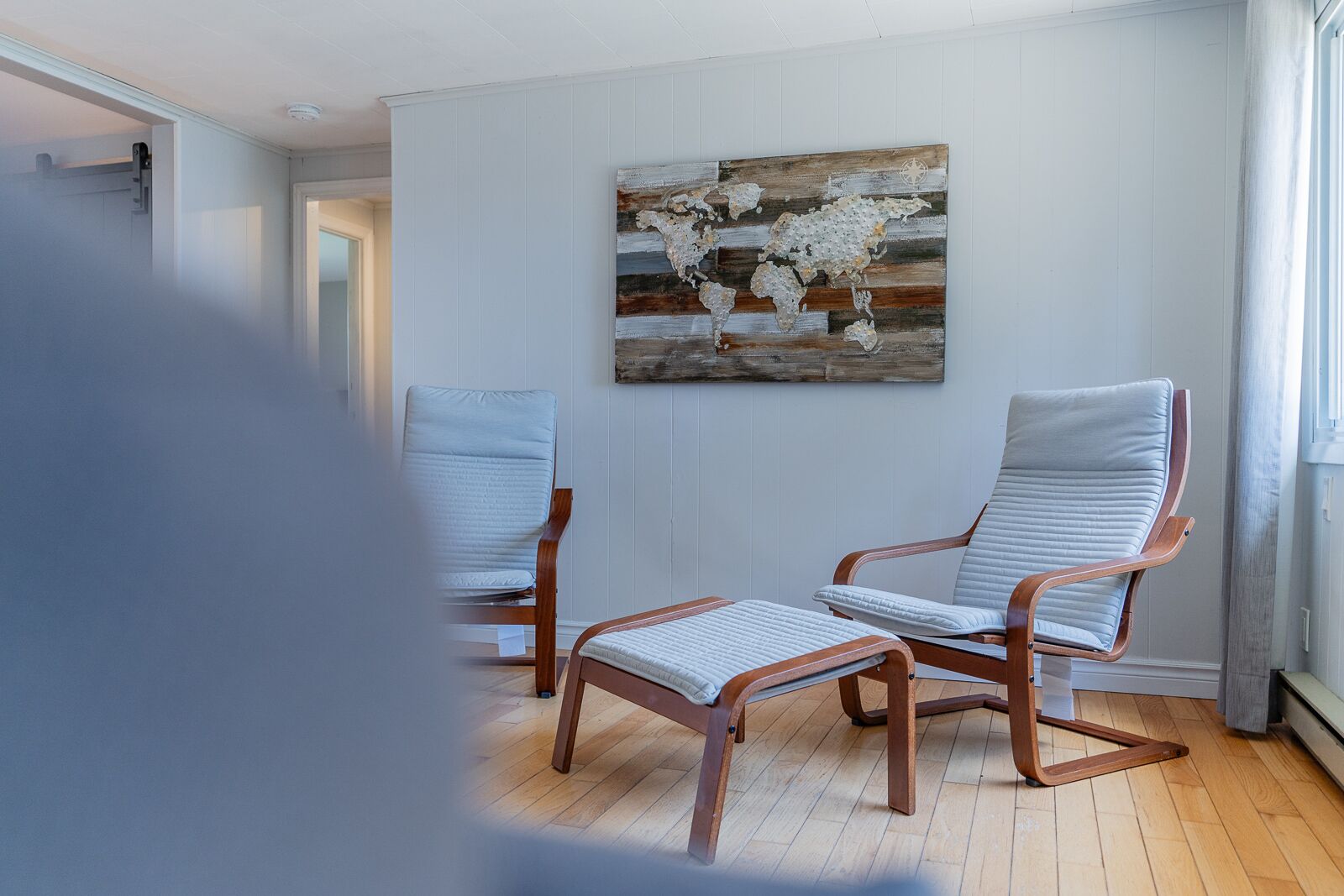 Ein Zimmer mit zwei Polstersesseln, einem Holztisch und einem Wandbild mit einer Weltkarte.