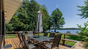 En træterrasse med et glasbord og stole, der vender ud mod en sø.