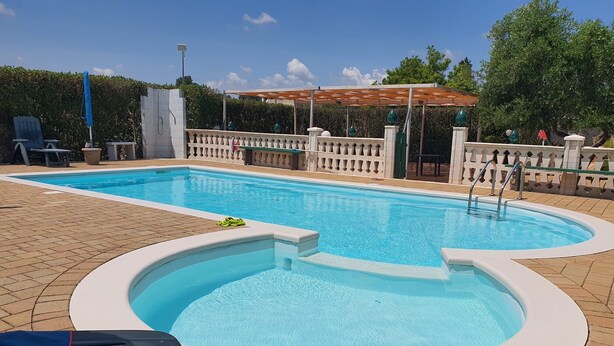 A rectangular swimming pool with a small hot tub, surrounded by a brick deck and a decorative fence.