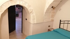 A bedroom with a bed, a small bedside table, and an arched doorway leading to another room.