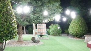 A well-maintained lawn with a wheelbarrow, string lights, and a neatly trimmed hedge.