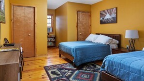 A room with two beds, a ceiling fan, a bookshelf, and a window.